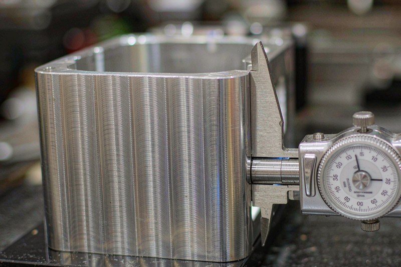 Digital caliper measuring the outside width of a machined aluminum housing on a granite plate