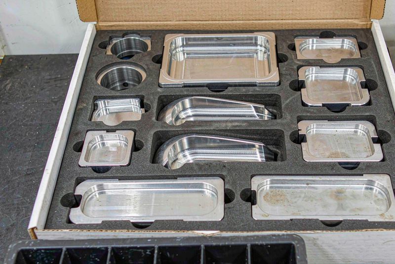 Machined aluminum and stainless parts nested in foam cutouts inside a shipping carton