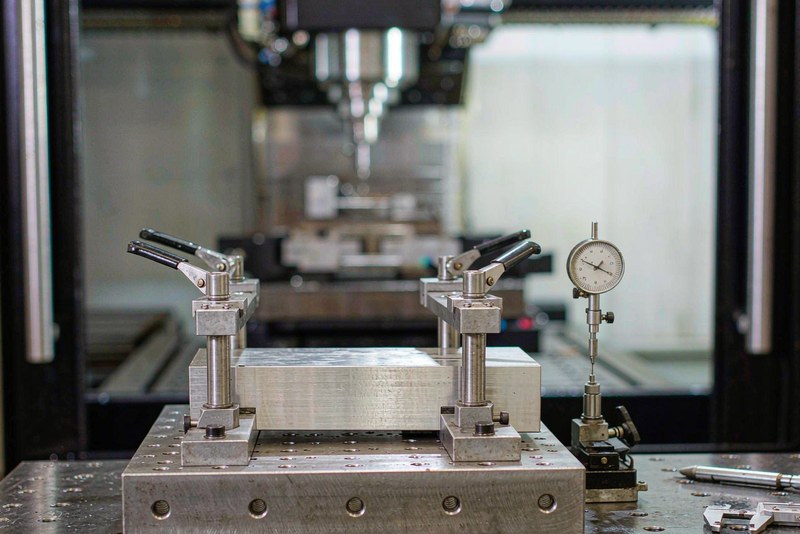 Aluminum workpiece clamped on a fixture plate with a dial indicator set against it