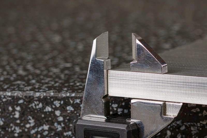Digital caliper measuring the thickness of a machined aluminum plate on a surface plate
