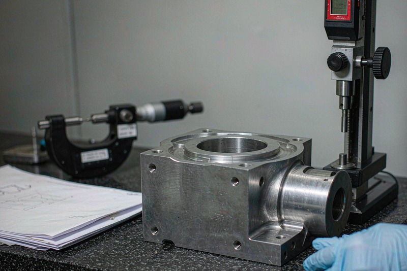 Technician checking a machined aluminum housing against a drawing on a granite surface plate