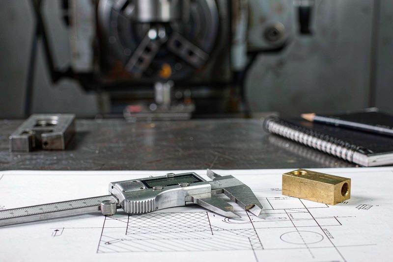 Printed engineering drawing with a caliper and a small machined block on a workbench