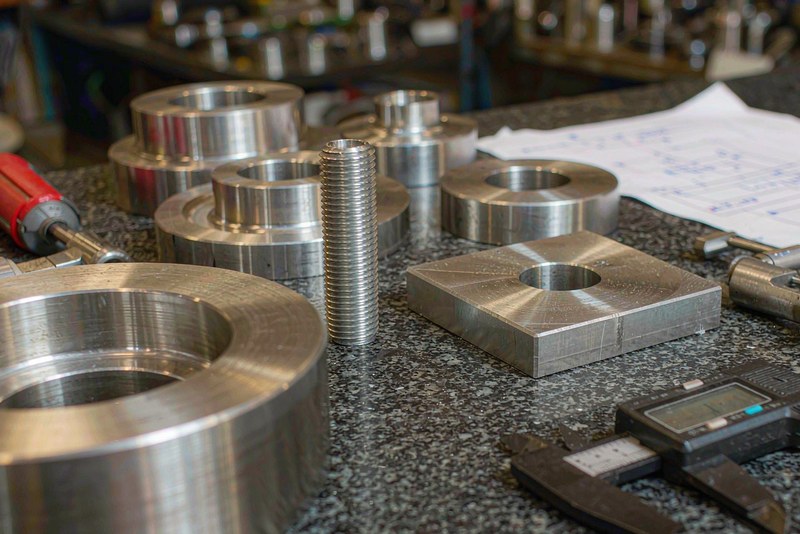 Machined rings and threaded fittings on a granite plate beside a digital caliper and a drawing
