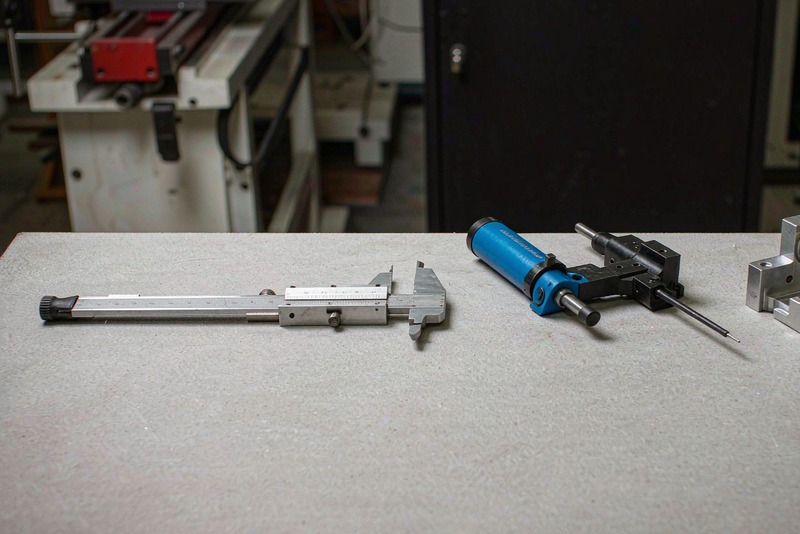 Outside micrometer and vernier caliper resting on a surface plate beside a machined part