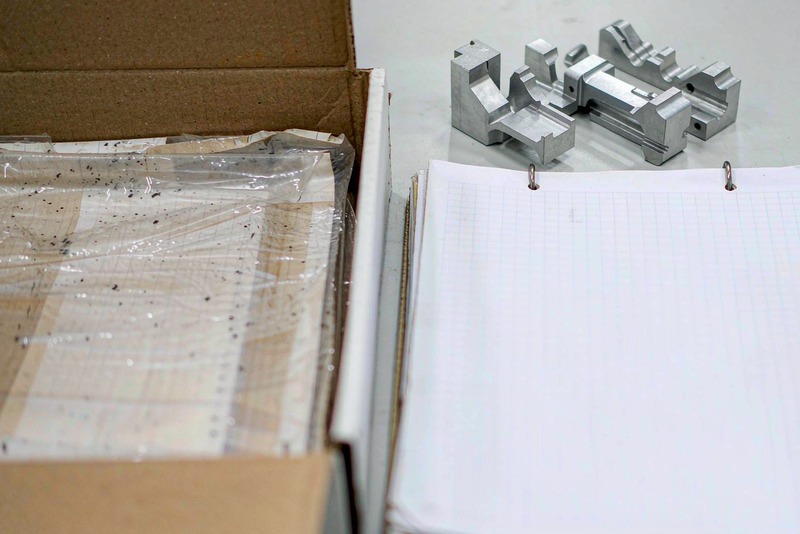 Machined aluminum parts on a bench beside printed inspection documents