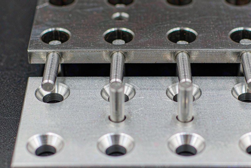 Machined plate lifted above a pinned plate showing the clearance gap