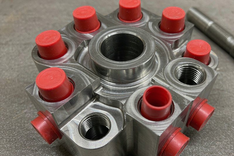 Aluminum manifold block with masked threaded ports beside a thread plug gauge