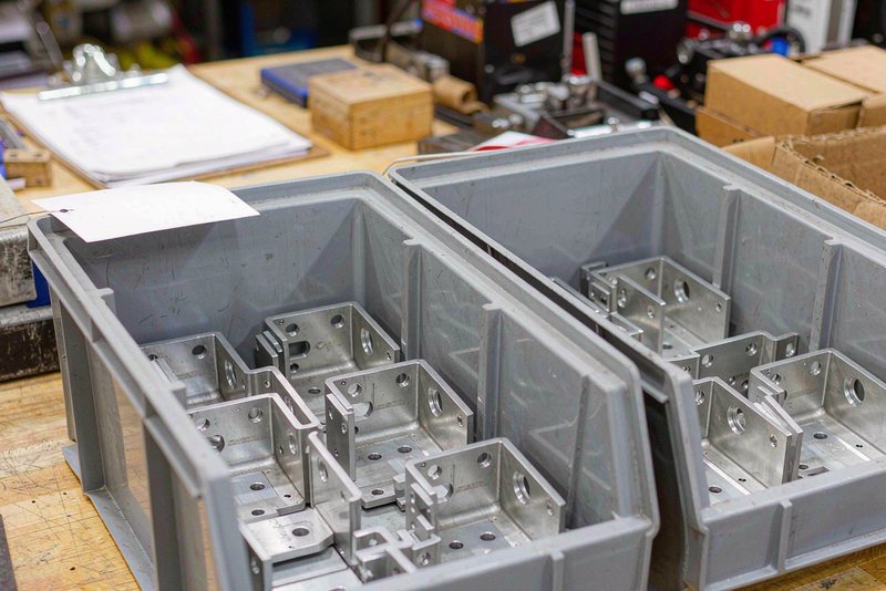 Two bins of identical machined aluminum brackets from separate production lots