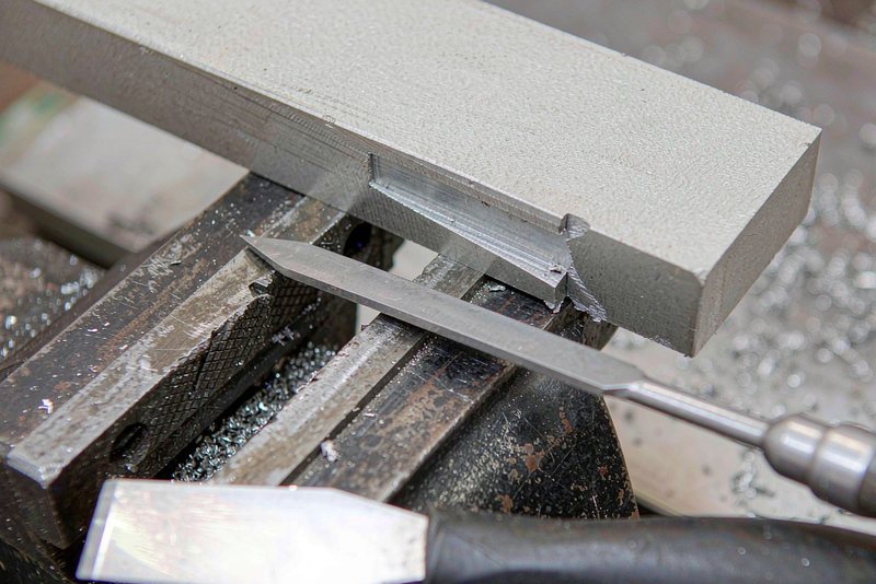 Machined aluminum part clamped in a bench vise being deburred by hand