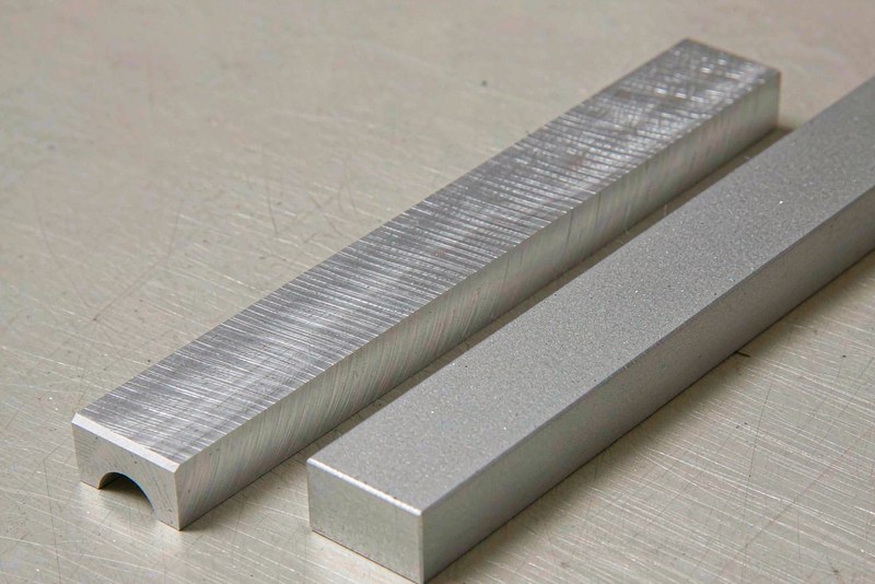 Two machined aluminum sample bars side by side, one with visible tool marks and one with a satin surface