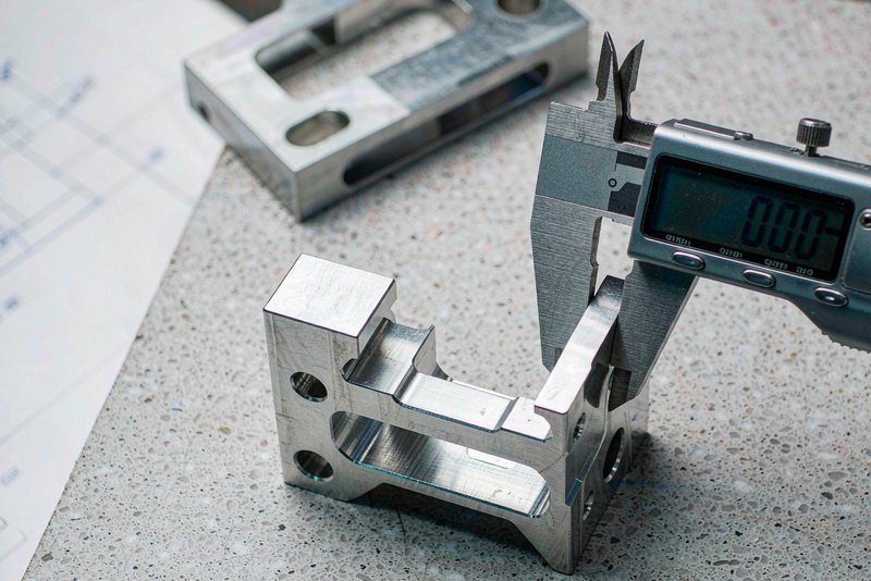 Digital caliper measuring the thickness of a machined aluminum bracket on a granite surface