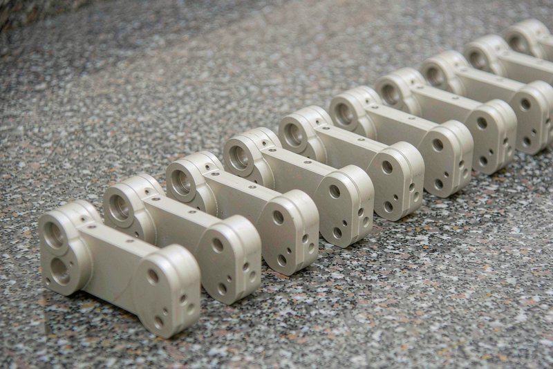 Ten identical machined aluminum brackets lined up on a granite surface plate