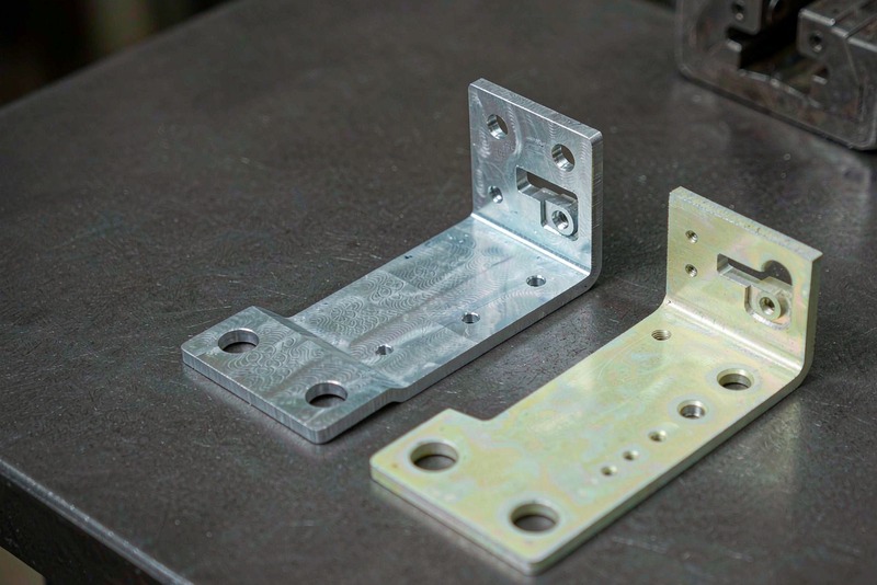 Two machined aluminum brackets showing clear and yellow iridescent conversion coating side by side
